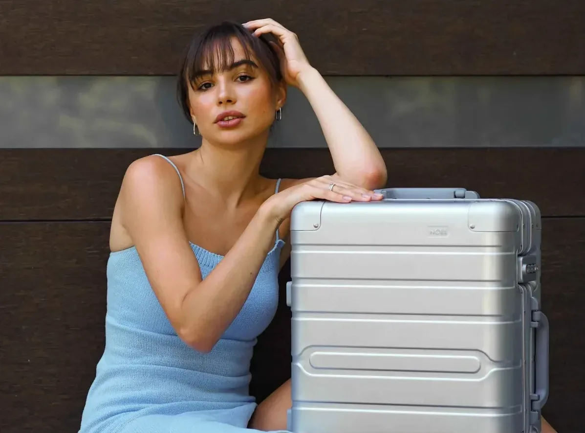 Woman leaning on a silver NOBL aluminium suitcase