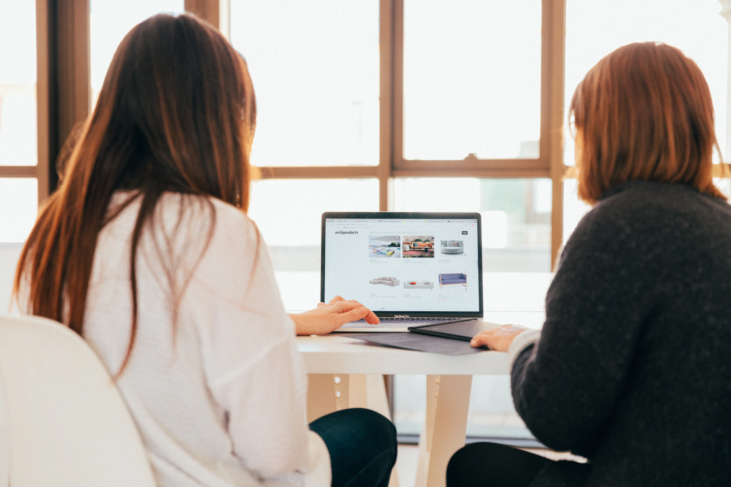 Two colleagues working together at a laptop by a sunny window